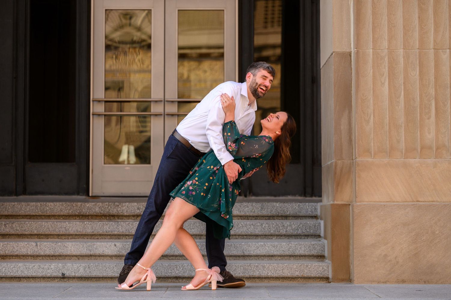 A couple in formal attire performs a romantic dance dip on the steps of a historic stone building.