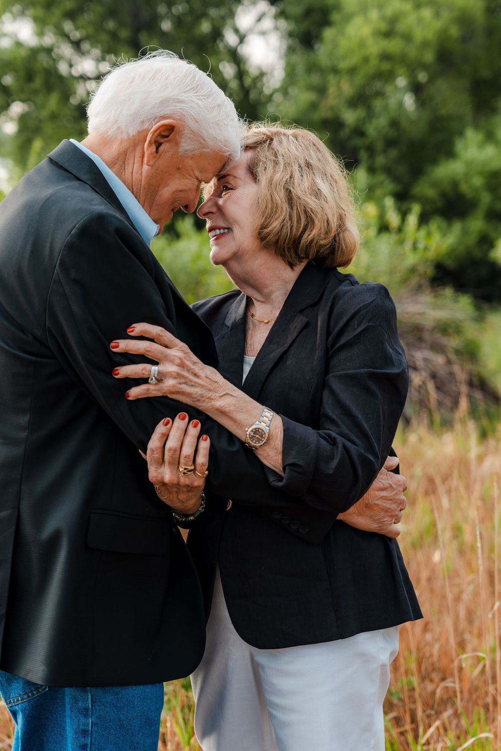 Elderly couple sharing a tender forehead-to-forehead moment outdoors, smiling and embracing in a lush green setting.