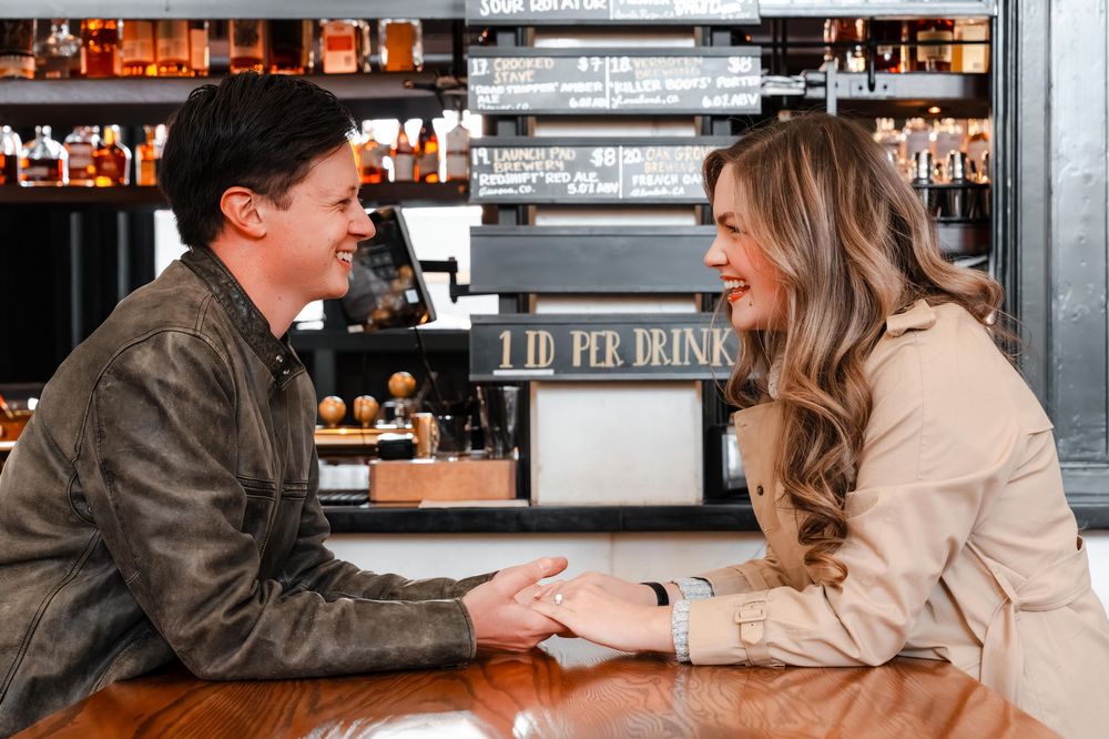 Romantic couple holding hands and talking across a bar counter at a stylish venue.