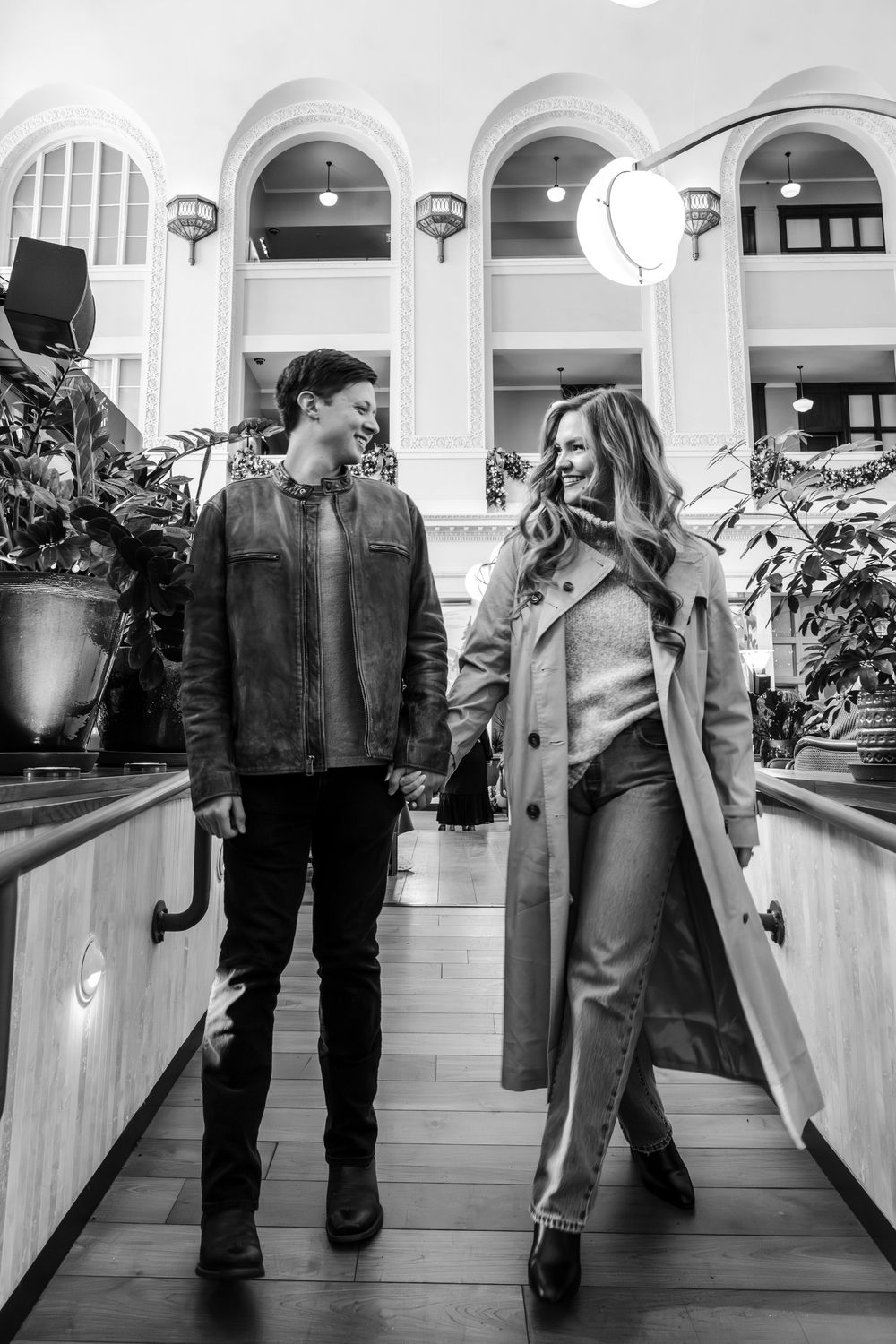 Black and white photo of a couple holding hands while walking through an elegant building.