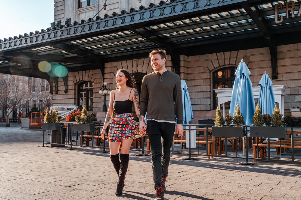 Stylish young couple walks together outside a urban restaurant patio on a sunny day.