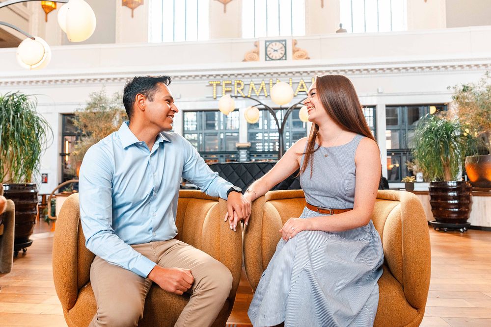 Couple sitting in leather chairs smiling at each other in elegant hotel lobby.