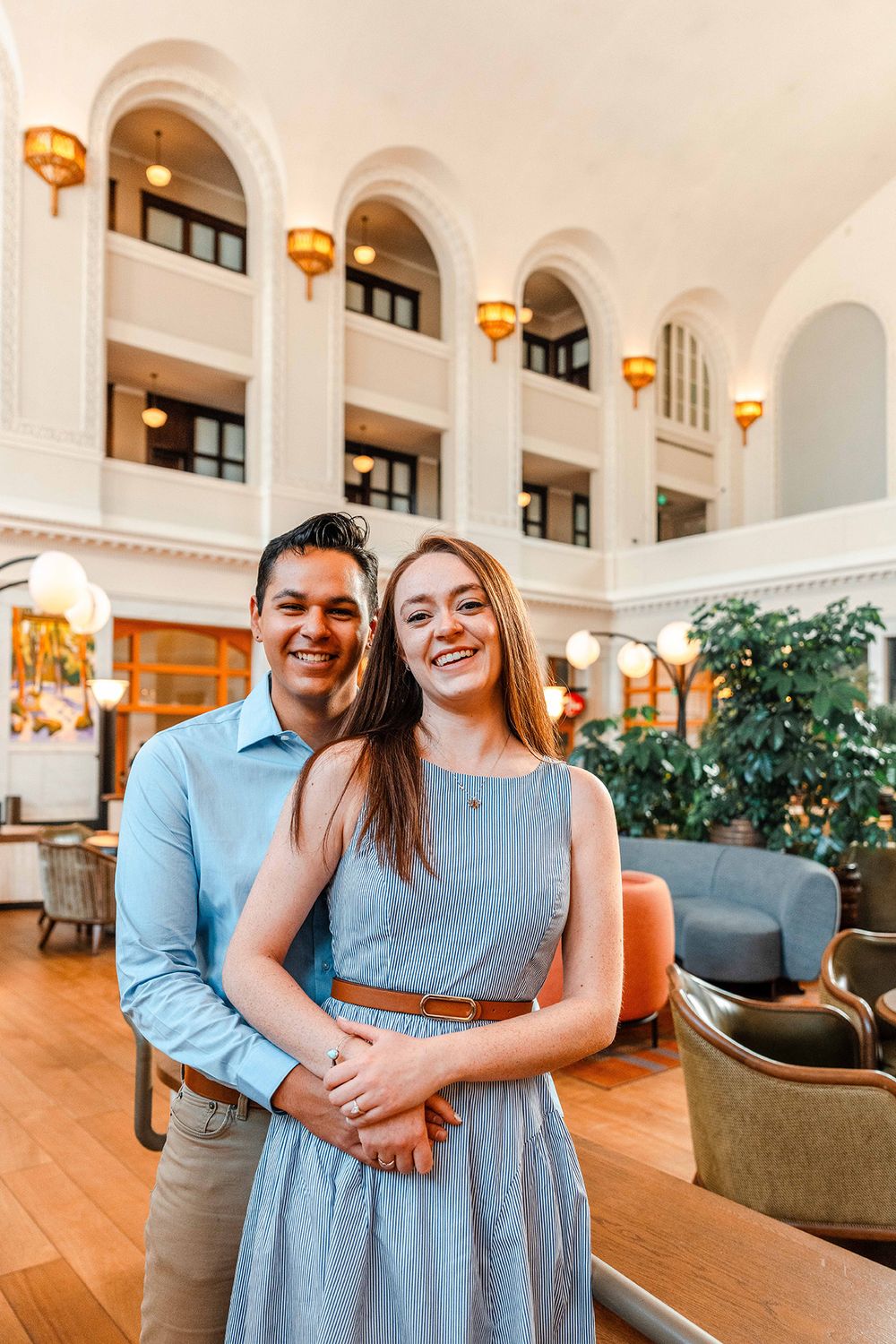 Smiling couple embracing in grand hotel atrium with arched white architecture.