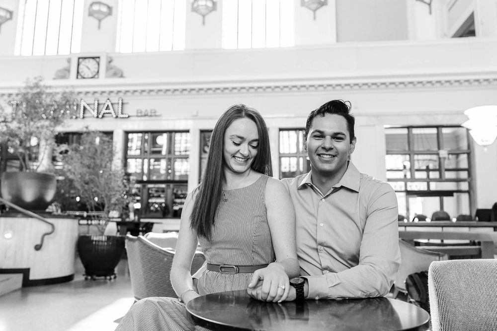 Black and white photo of couple holding hands and laughing at bar table.