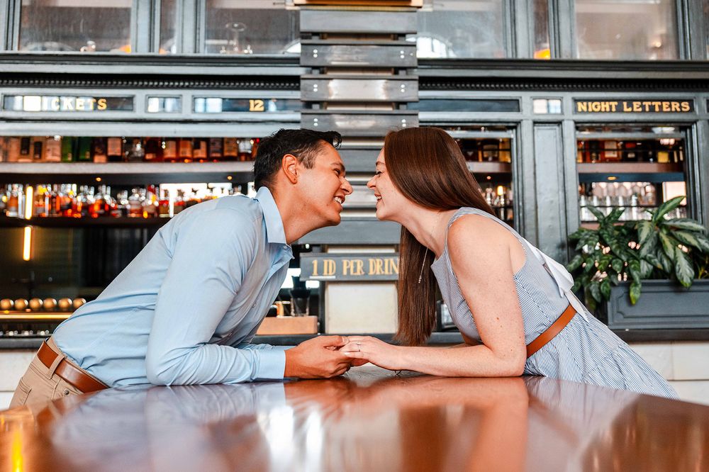 Romantic couple leaning toward each other across wooden bar counter holding hands.