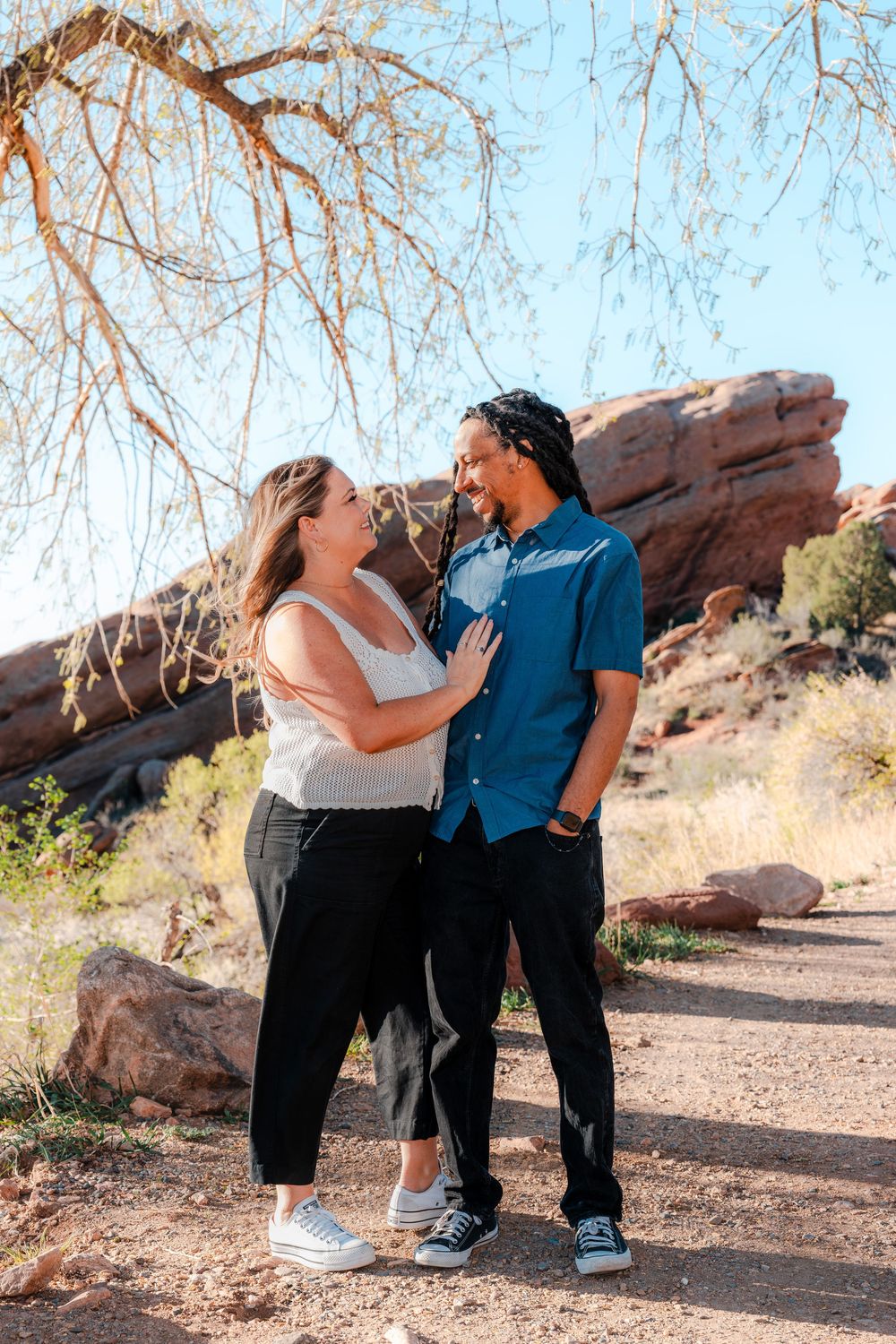 Couple smiling at each other outdoors at Red Rocks Park, Colorado, surrounded by red rock formations and desert landscape.