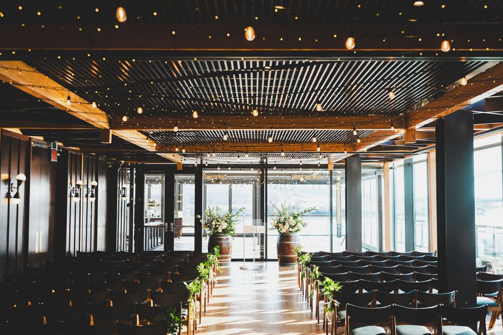 Modern dc ceremony space with exposed wood beams, string lights, and floor-to-ceiling windows creating an open, airy atmosphere.