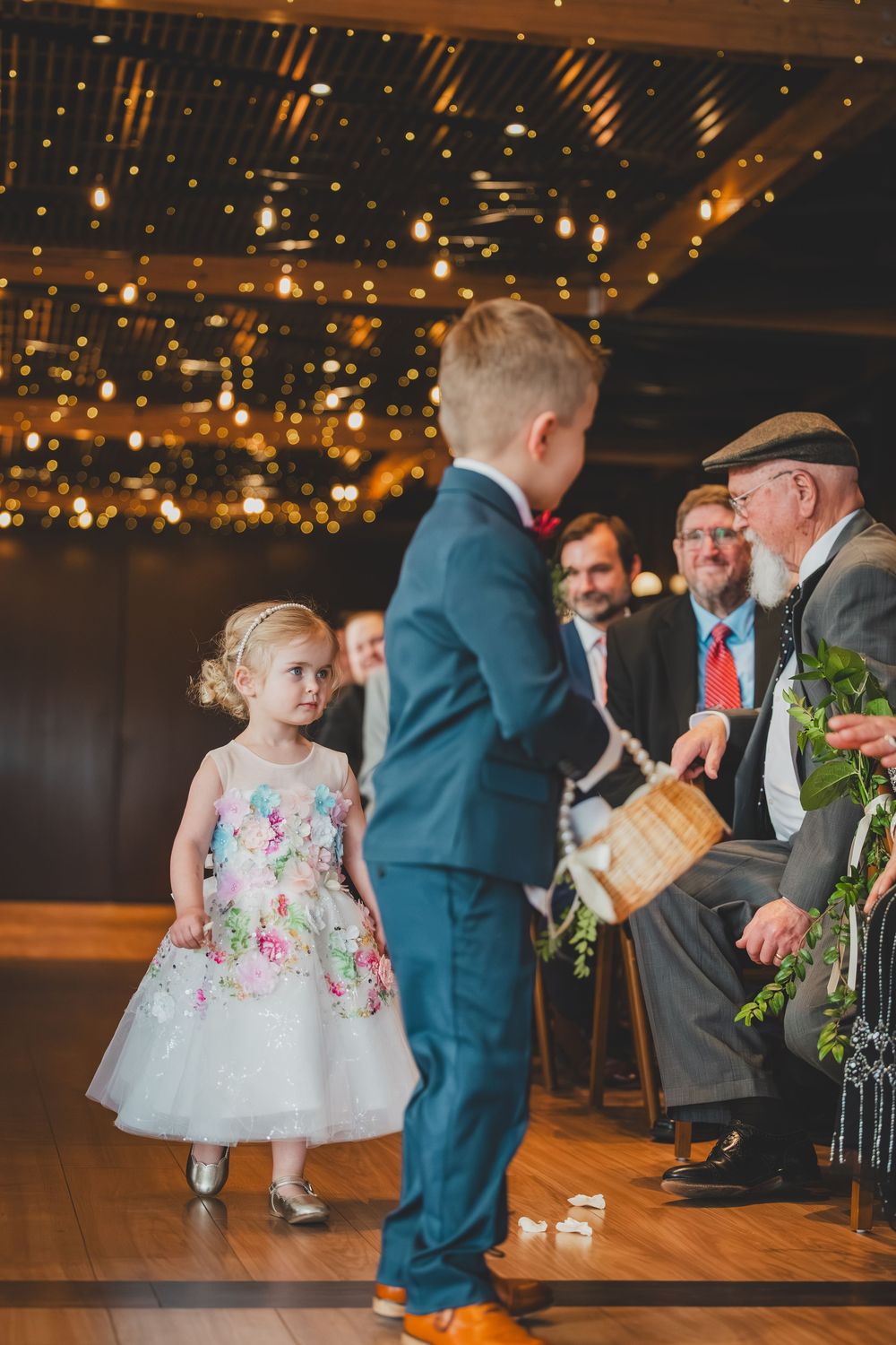 A young child in a floral dress twirls and dances at a wedding reception under warm lighting.