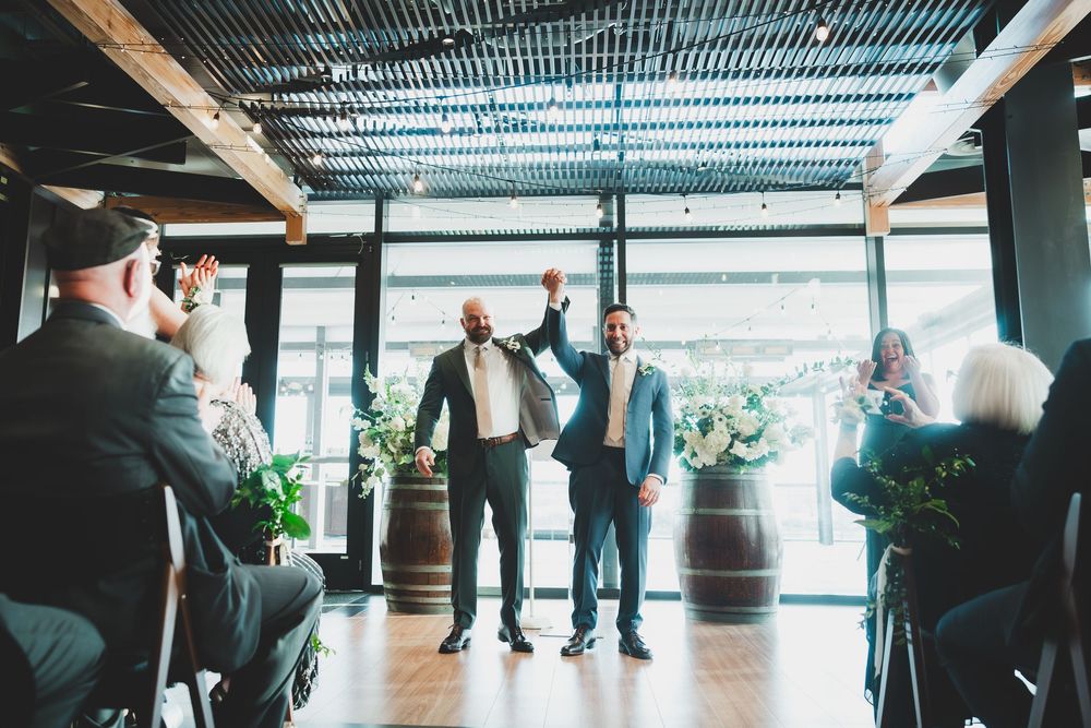 Grooms raising their hands up the air celebrating their union at the District Winery in DC