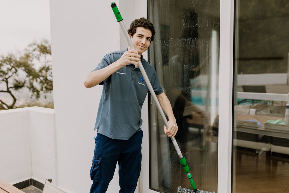 Photo of Tom cleaning low window crystals with his long special stick looking at the camera.