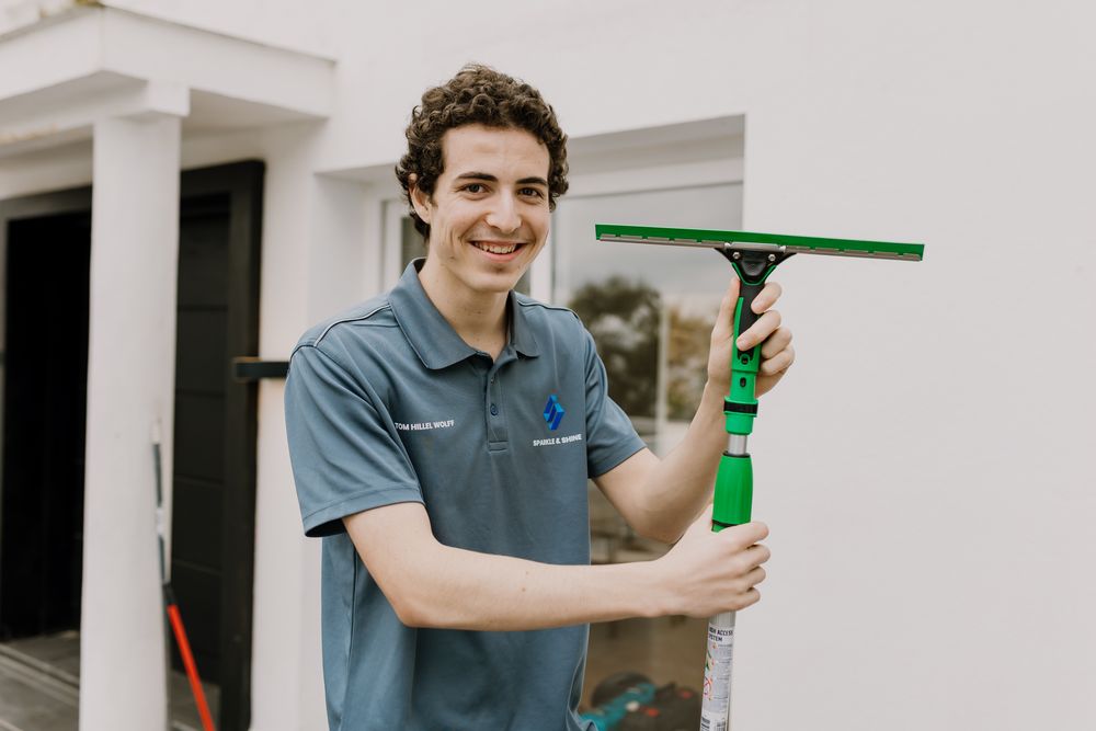 Photo of Tom holding his window wiper connected to a long stick, looking at the camera.