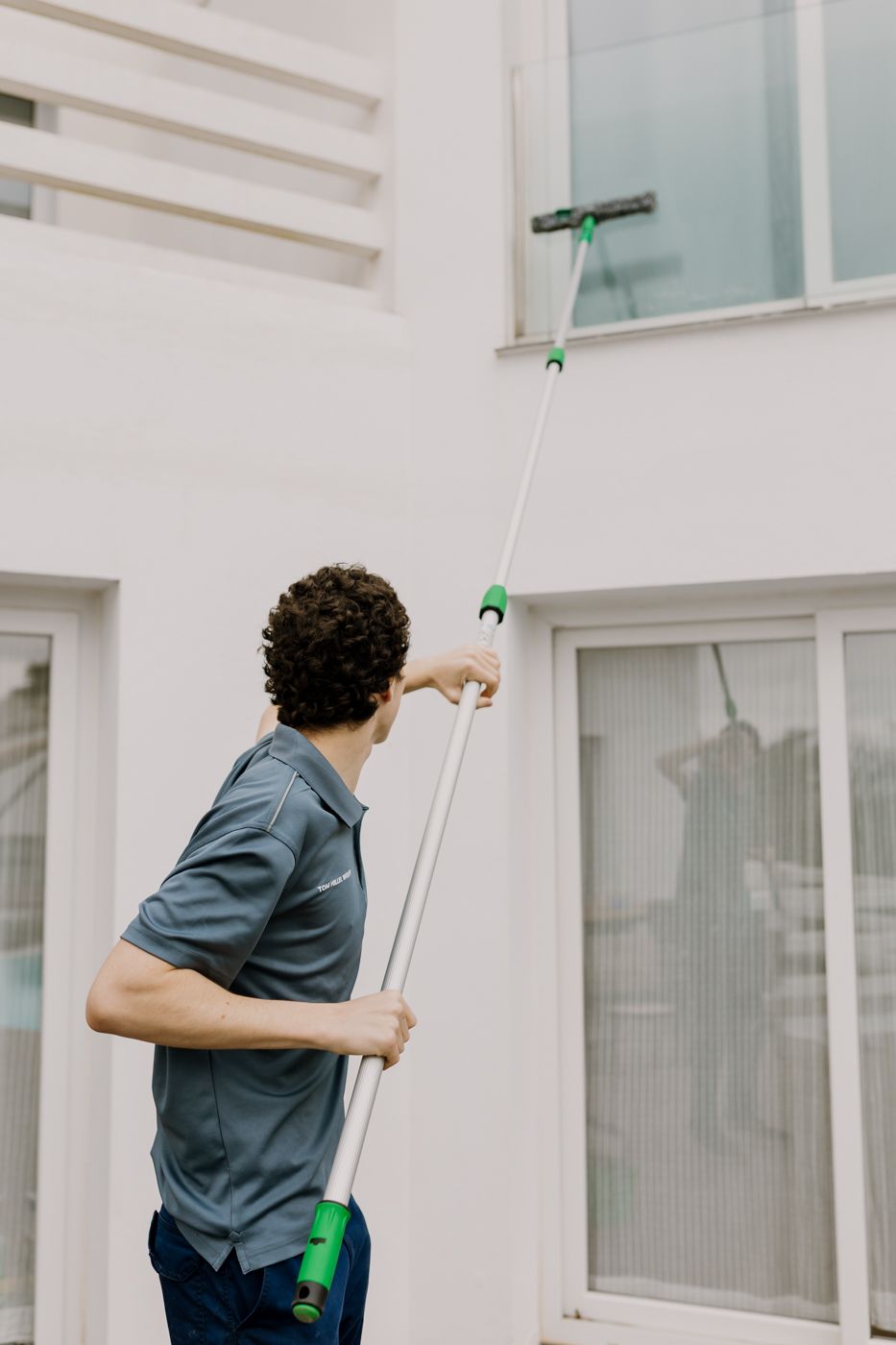 Photo of Tom cleaning a high window crystals  with his long special stick looking at the window.