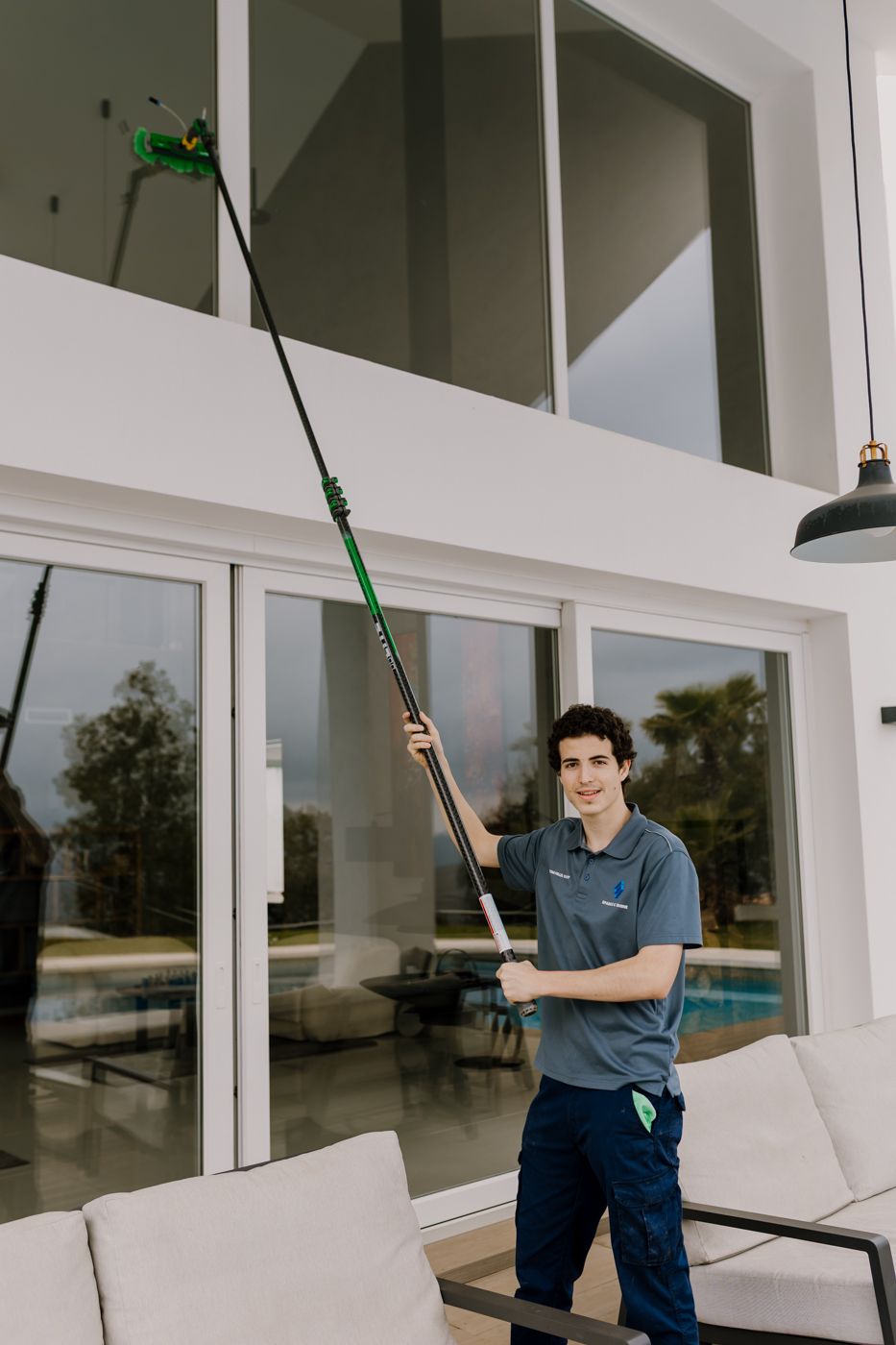 Photo of Tom cleaning a high window crystals  with his long special stick looking at the camera.