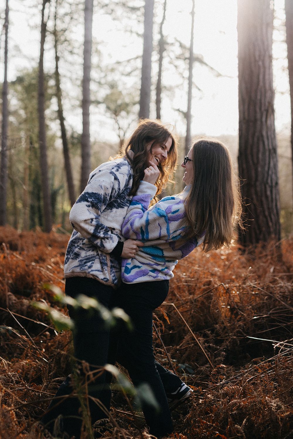 Two people playfully interact in a forest setting with autumn ferns covering the ground.