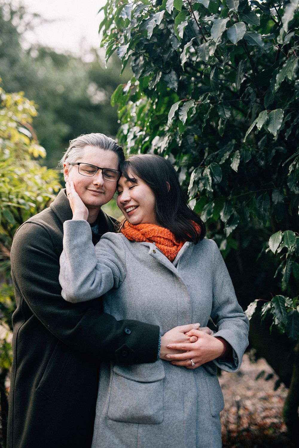 A couple shares intimate laughs together among green vines during an outdoor photoshoot.