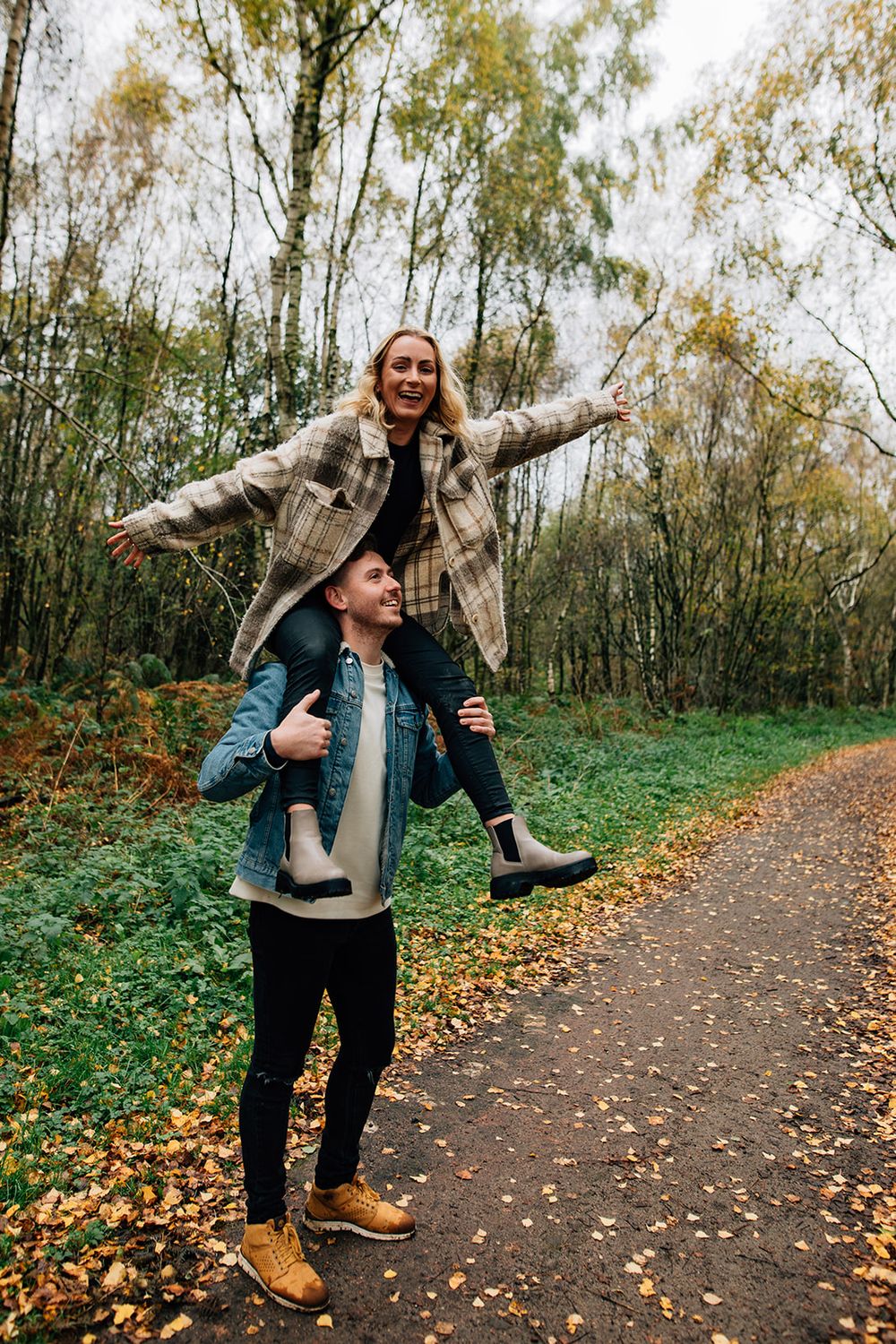Person playfully jumping and posing on an autumn path lined with trees and fallen leaves.