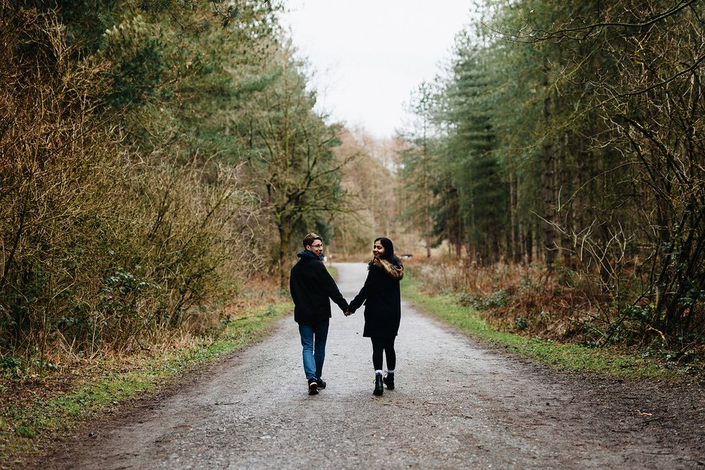 A couple walks hand in hand down a tree-lined path during autumn.