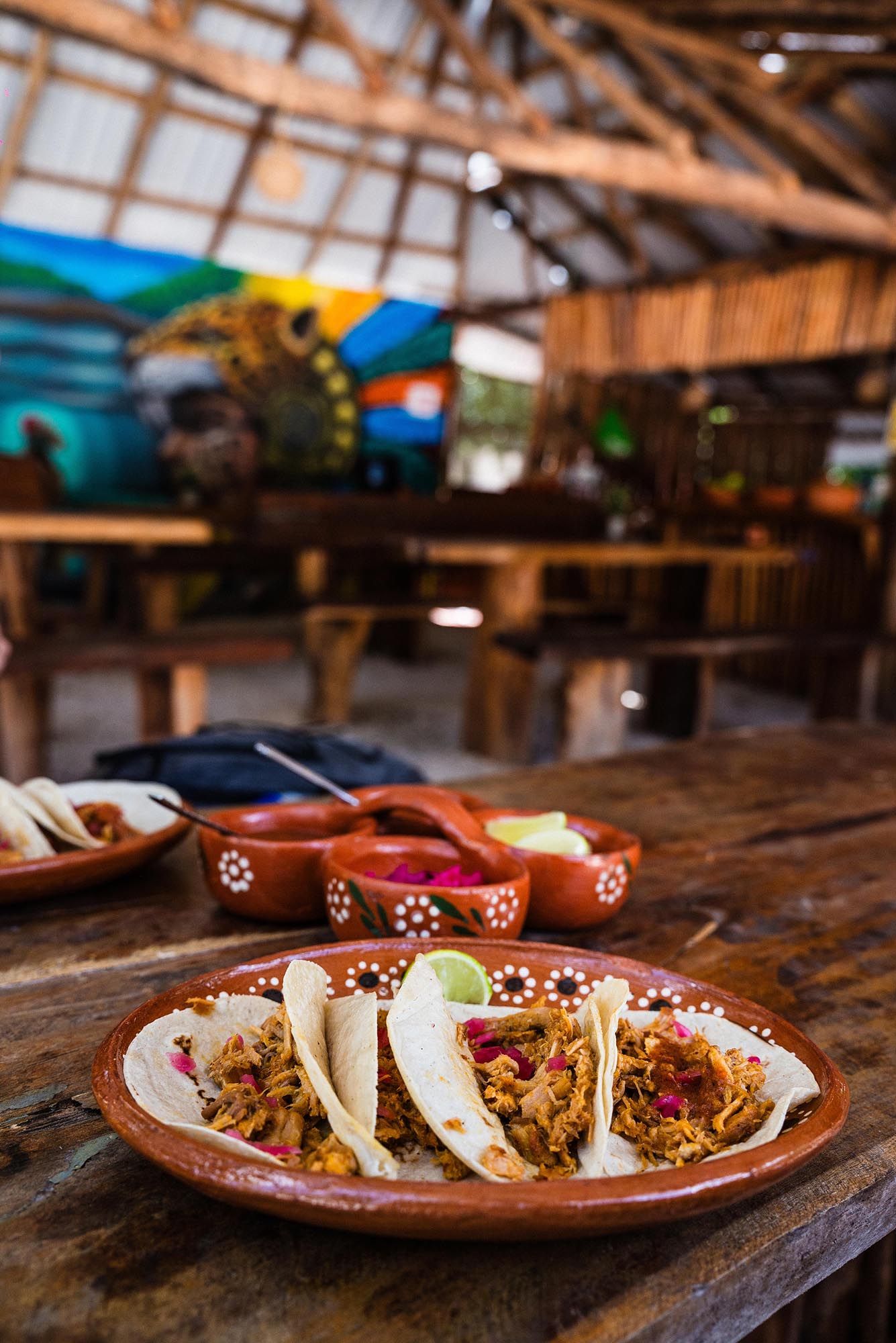 Three authentic Mexican street tacos served on a rustic wooden table with garnishes on a traditional clay plate.