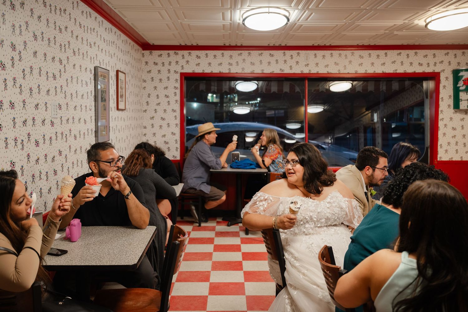 A crowded dance class learns salsa steps in a studio with checkered walls and overhead lighting.