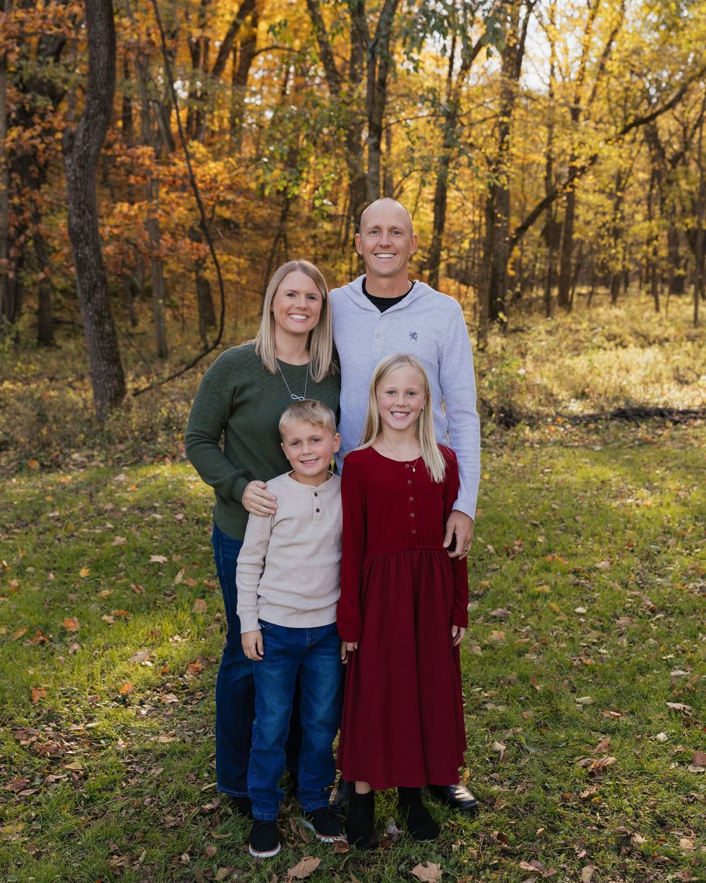 Family group poses together outdoors in autumn forest setting with golden fall foliage in background.