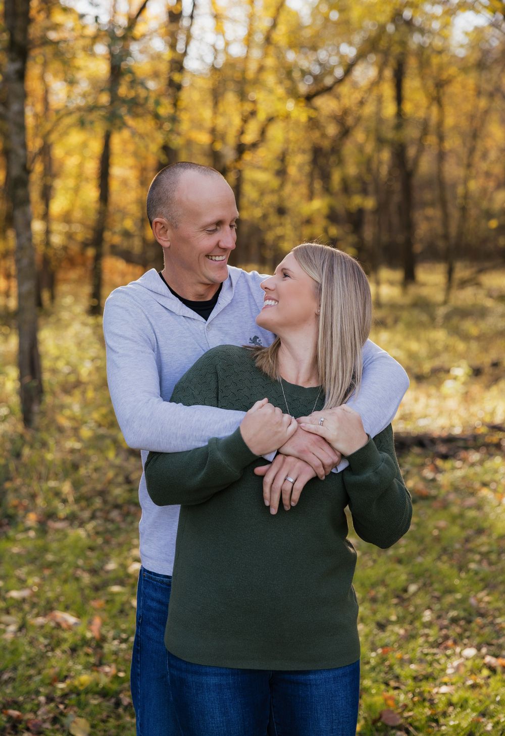 Couple embracing and laughing together in a sunlit autumn forest with golden foliage in the background.