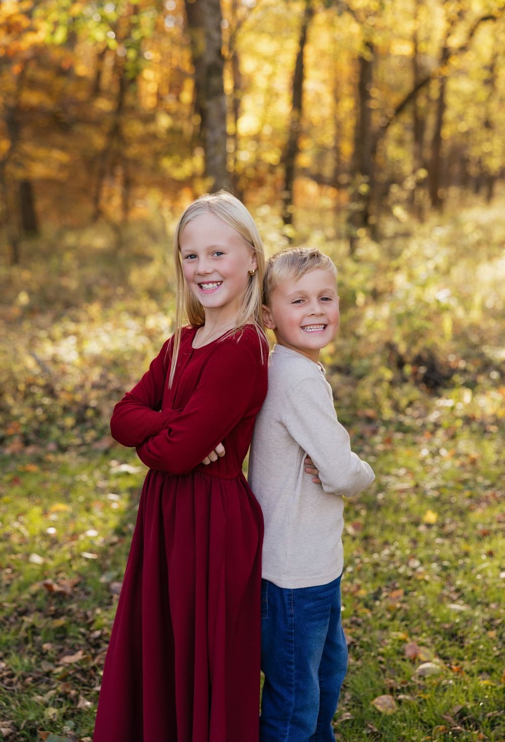A playful autumn photoshoot in a golden forest with two siblings in burgundy and cream outfits.