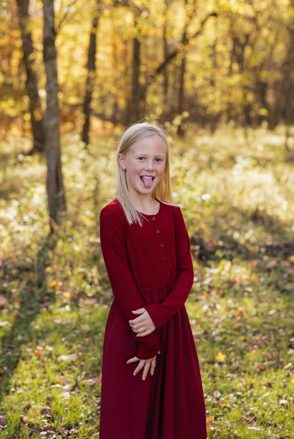 A series of four playful poses in a burgundy dress against a golden autumn forest backdrop.