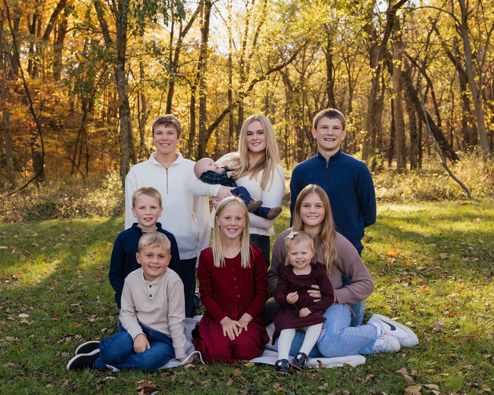 A group sits together outdoors for photos during autumn with golden leaves and trees in the background.