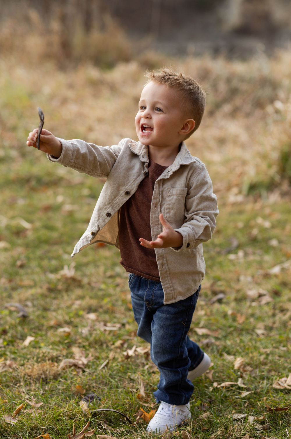 A toddler in jeans and light jacket plays energetically outdoors in the fall.