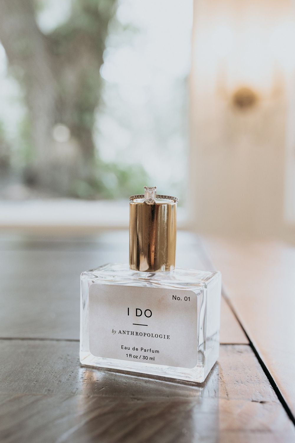 An elegant perfume bottle with minimalist design and gold caps displayed on a light marble surface in soft lighting with an engagement ring.