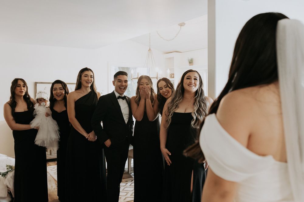 A group of bridesmaids wearing black attire gather together and see the bride for the first time at The Oaks at Duncan Lane.