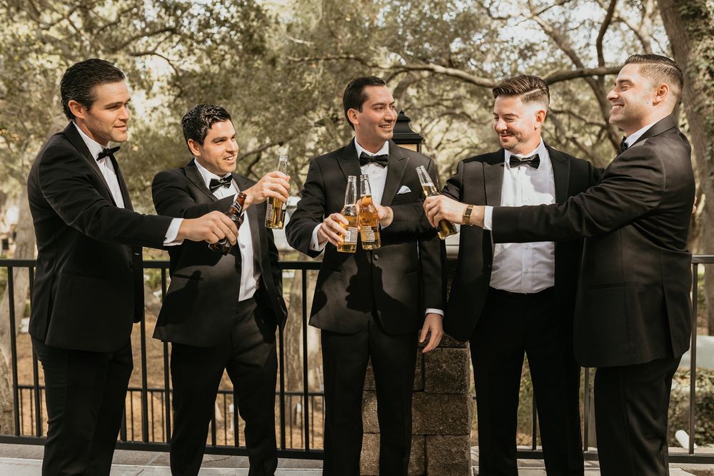 A group of groomsmen in black tuxedos toast at an outdoor wedding venue The Oaks at Duncan Lane.
