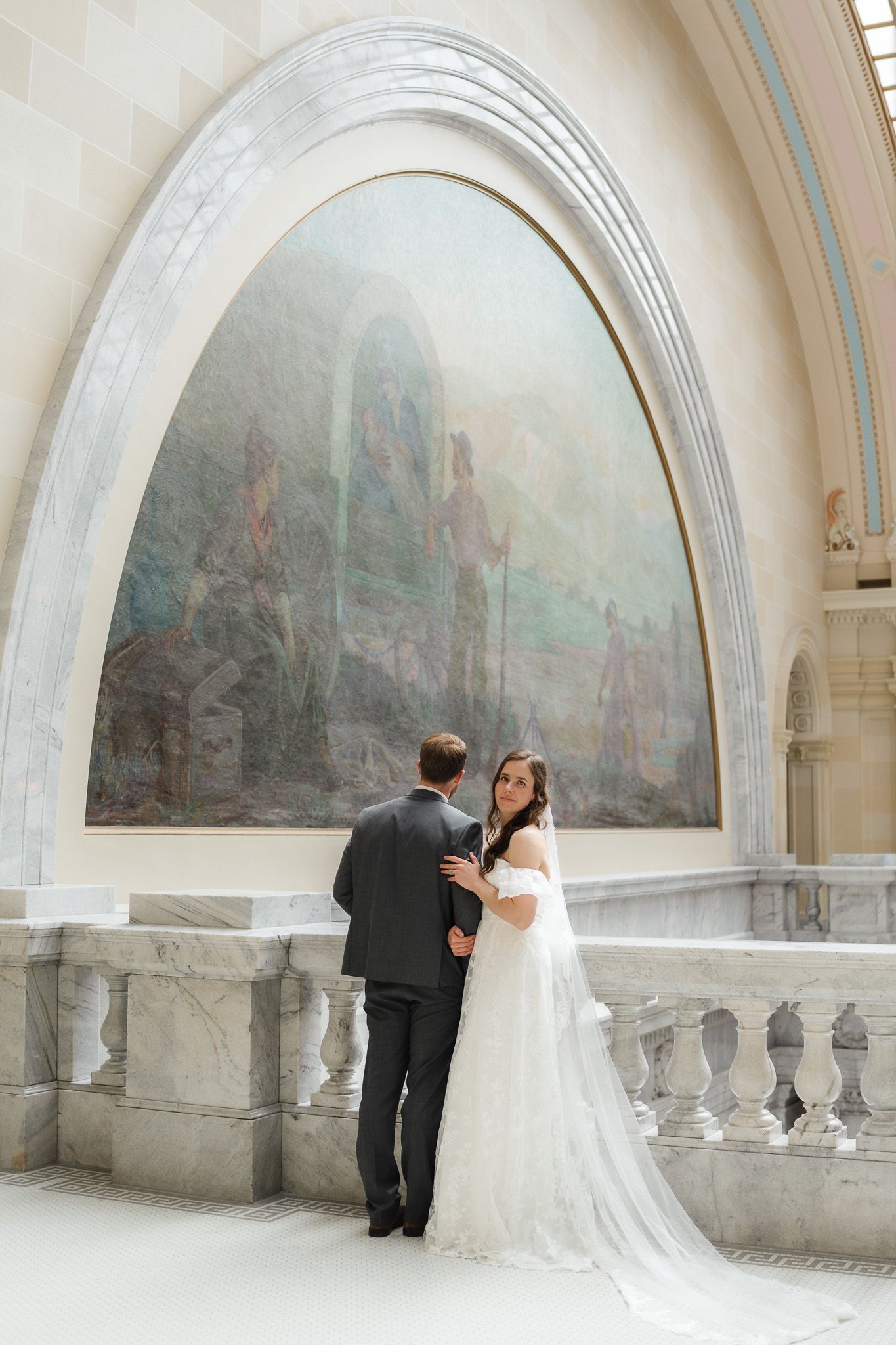 Elegant wedding couple poses under ornate stone archway with painted murals.