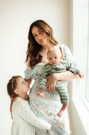 Mother and children in floral dresses sharing playful moments by bright windows.