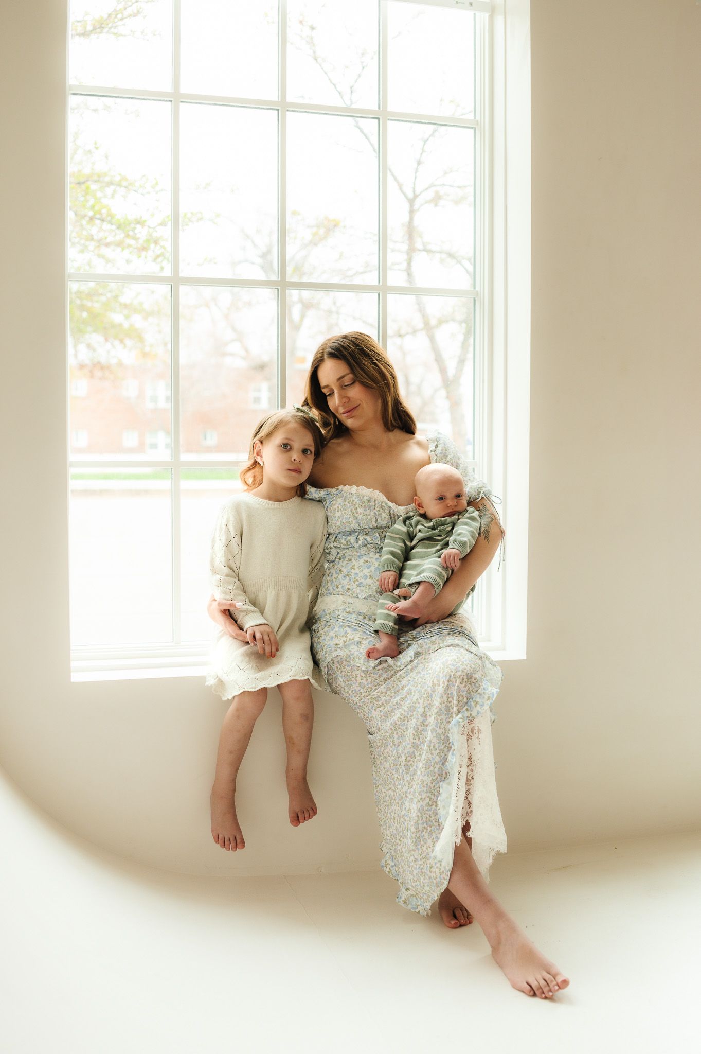 Soft natural light family portrait by window in white minimalist setting.