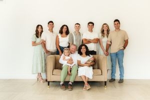 Group portrait of people in casual attire gathered around a beige couch against a white wall.