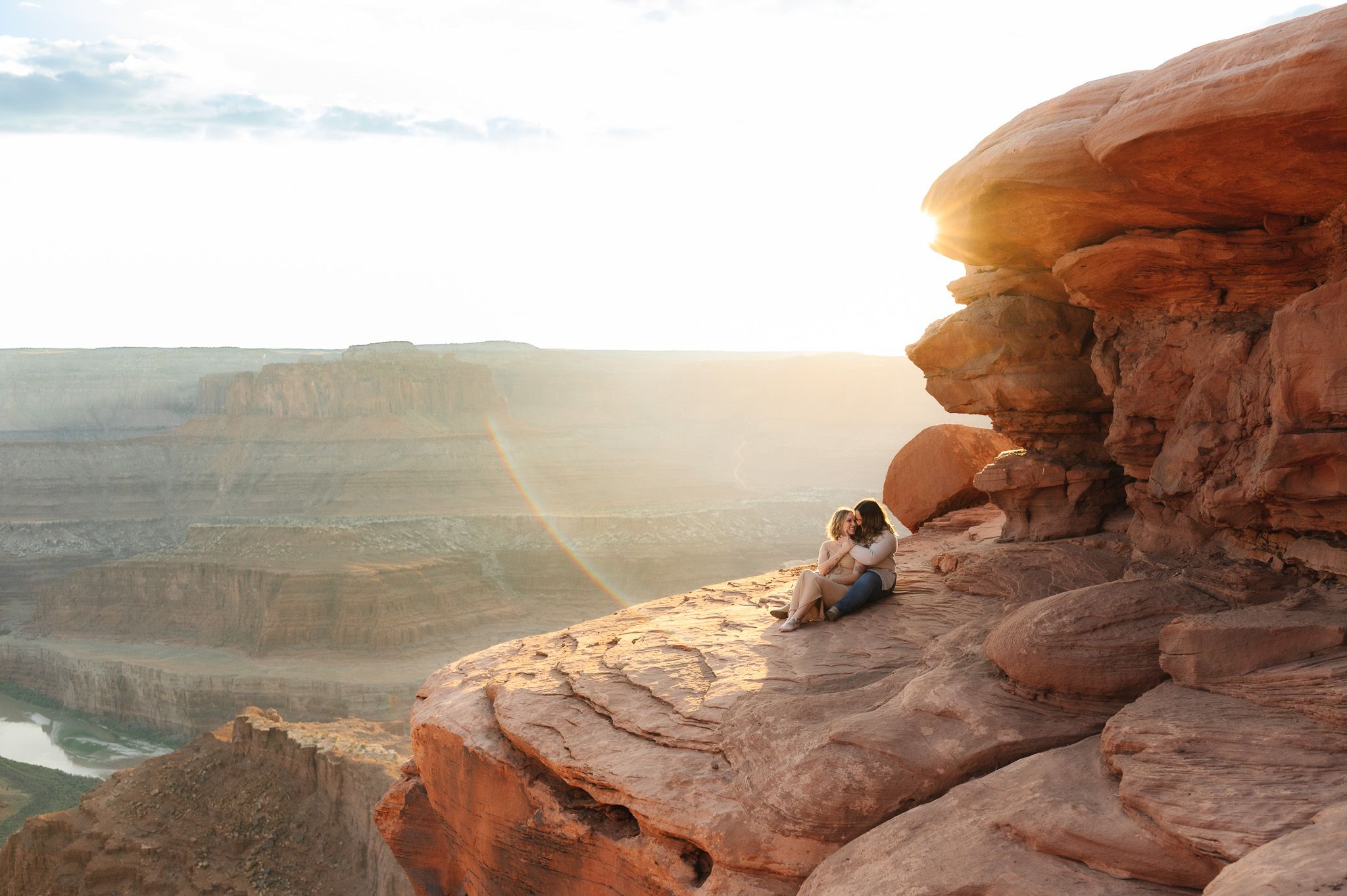 Romantic sunset photoshoot on red rock formations overlooking a desert landscape.