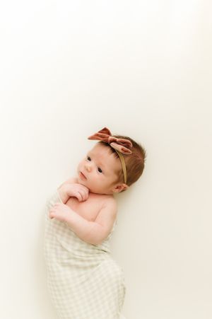 Newborn baby wrapped in cream blanket smiling against white background.