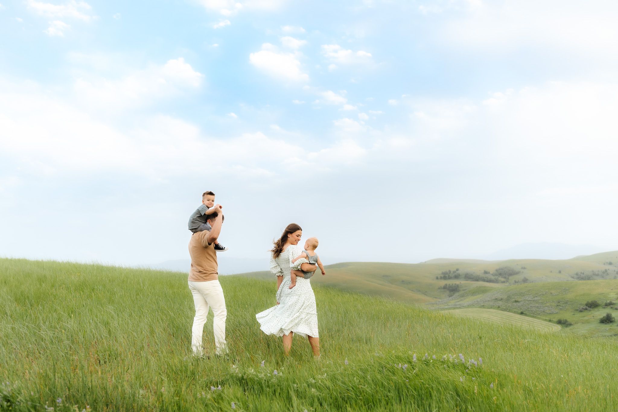 Family playing and dancing together on a green hillside under blue skies.