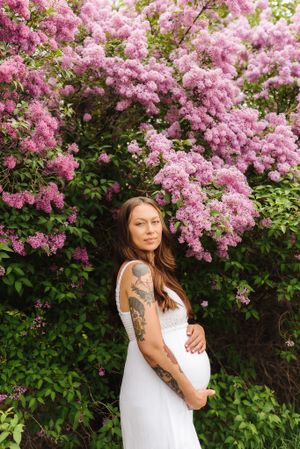 Maternity portrait with flowering pink lilac bush creating a romantic spring backdrop.