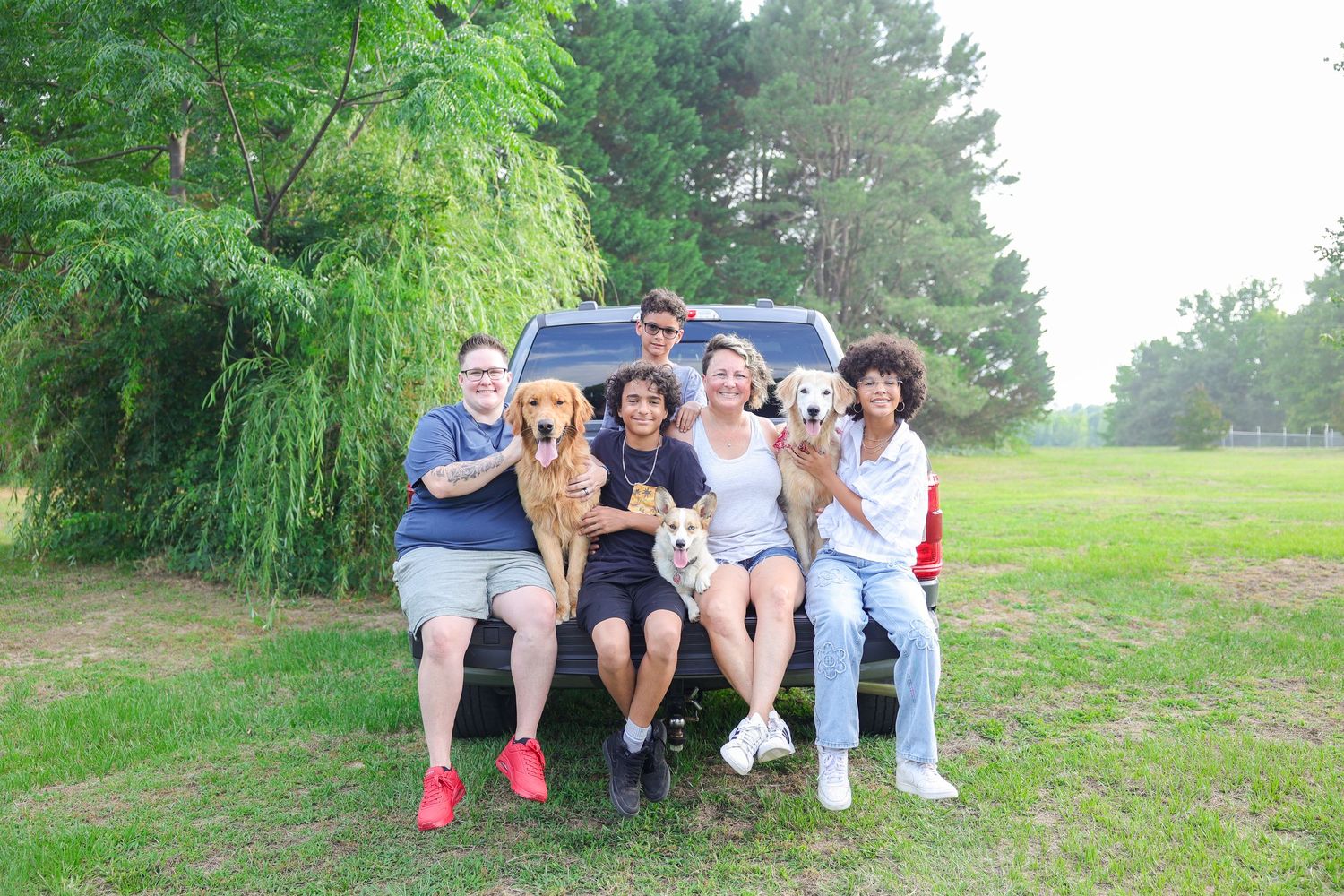 Family and dogs relaxing together on grassy hillside during outdoor photo session (Angier, NC).