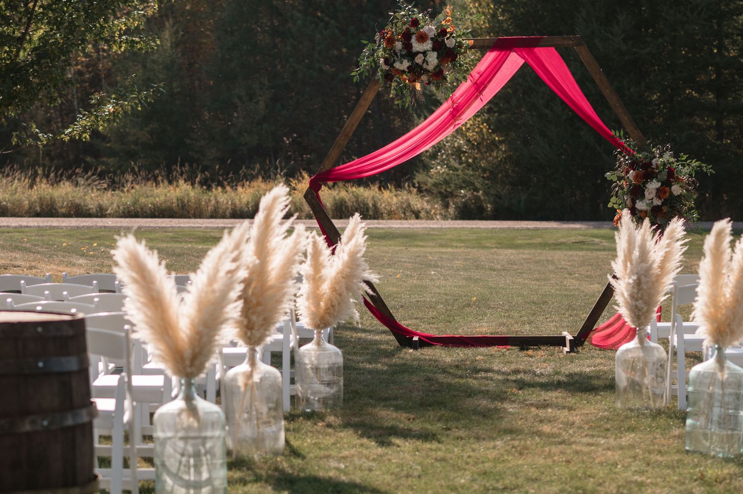Outdoor wedding ceremony setup with pampas grass in mason jars and bright pink fabric arch on a sunny day.