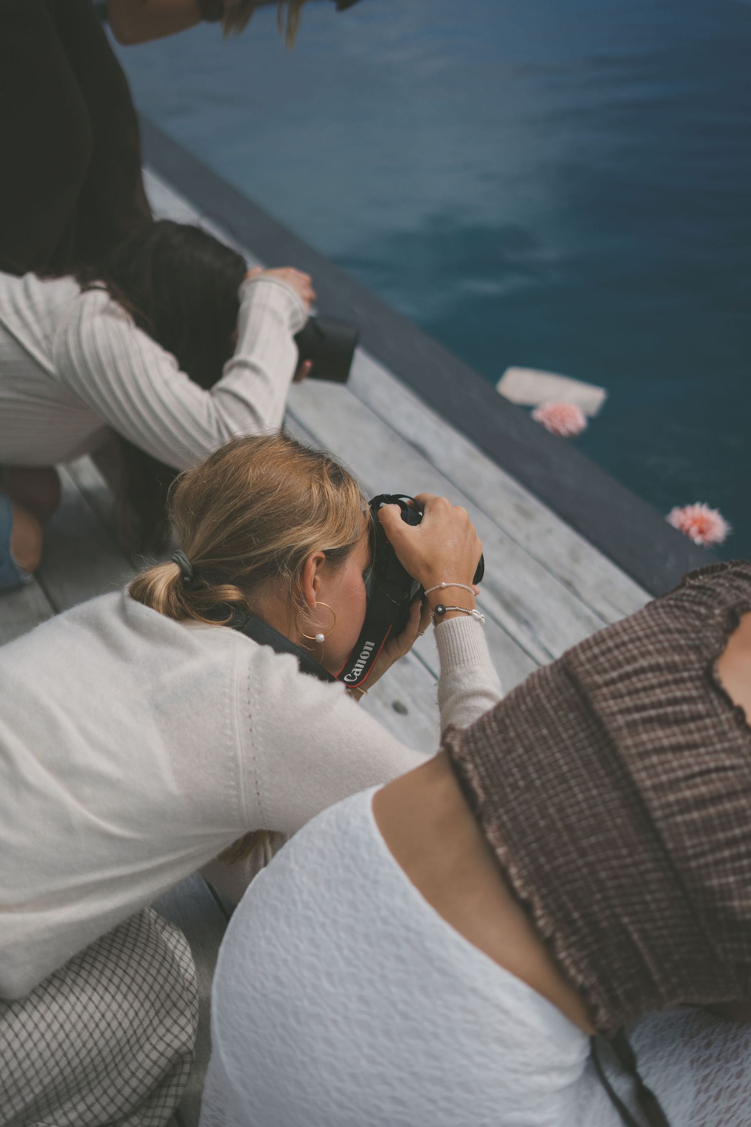 Photographer lying on a dock captures close-up shots of flowers floating in turquoise water.