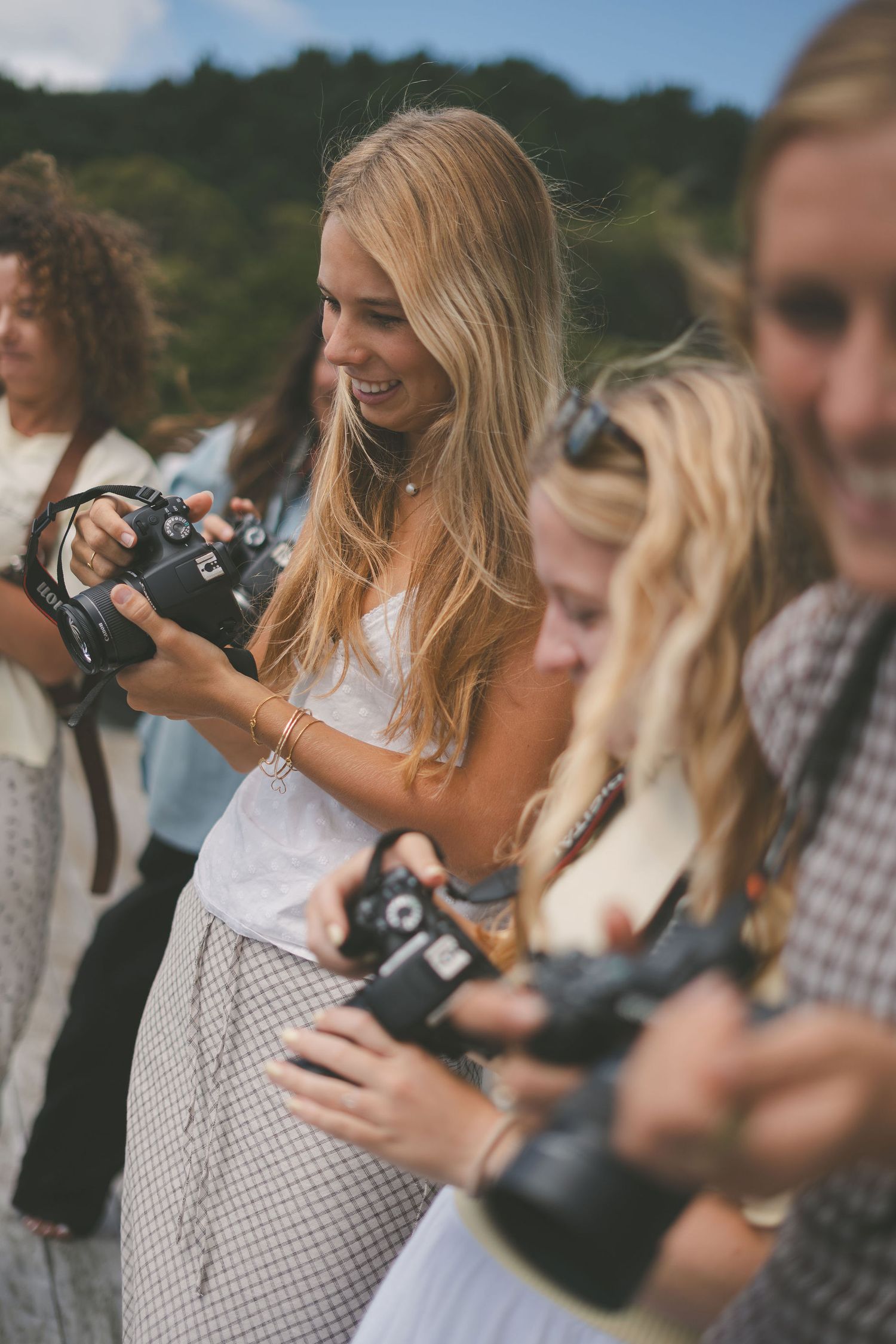 Group of smiling women reviewing photos on film cameras outdoors at a photography workshop.
