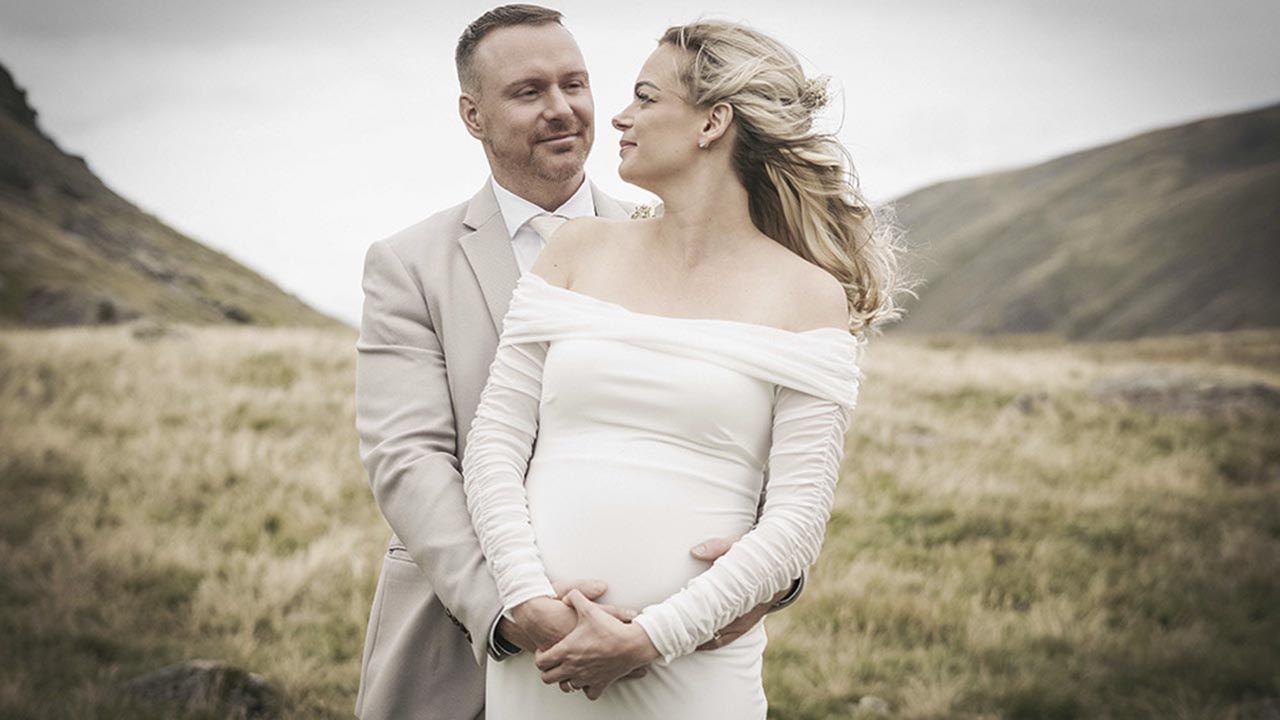 A romantic wedding couple embraces in a scenic mountain landscape with soft lighting and natural surroundings.