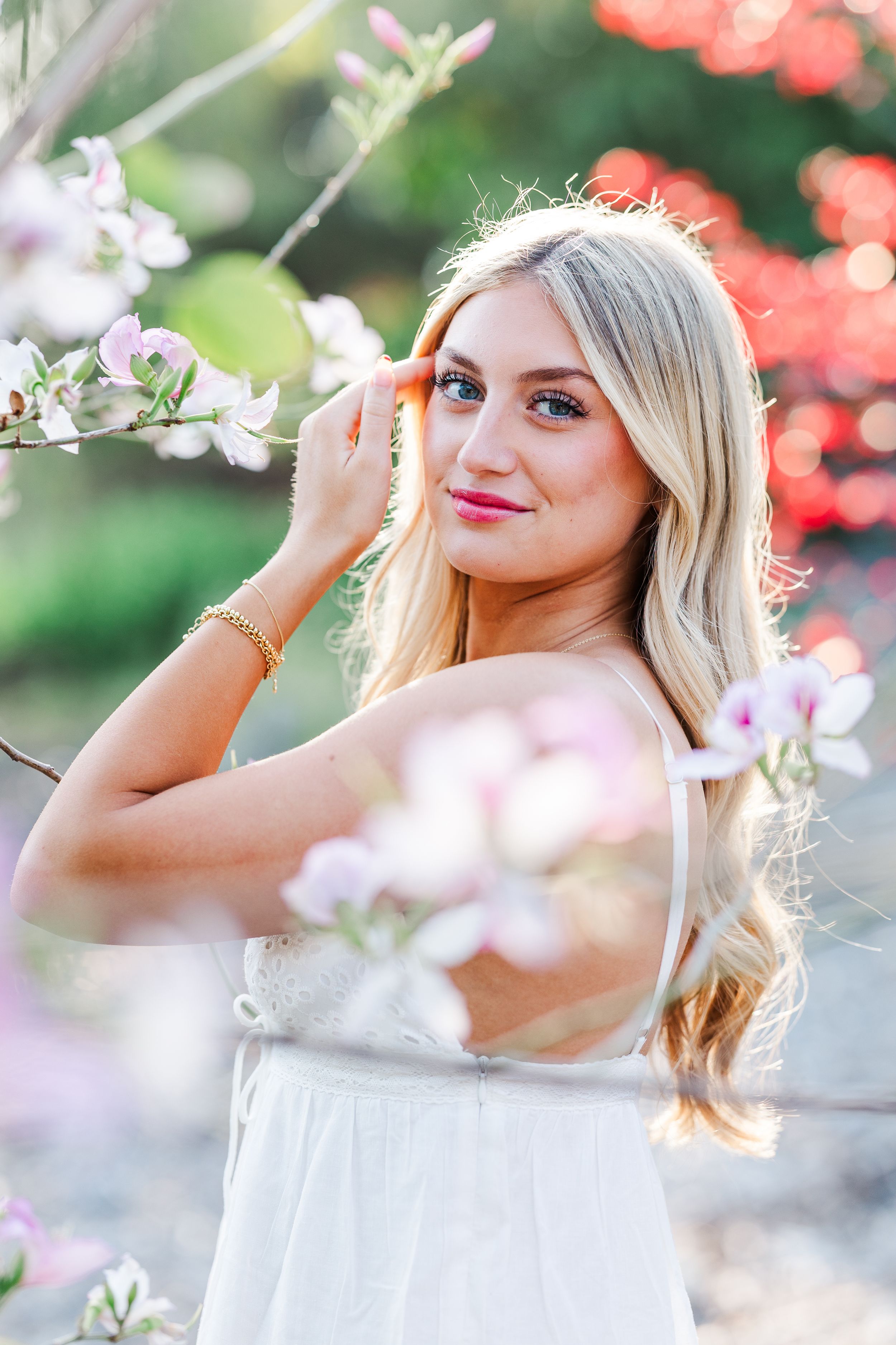 Spring portrait in white dress among cherry blossoms with soft bokeh background and pink floral accents.