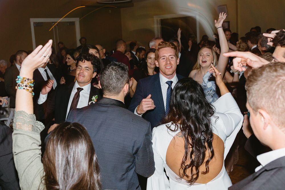 Wedding guests dancing and celebrating on a crowded dance floor at an evening reception.