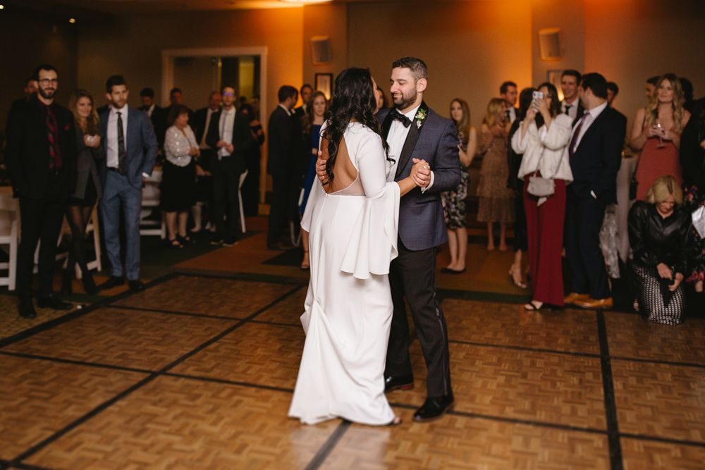 Guests gather around the dance floor at an elegant wedding reception in a dimly lit ballroom.
