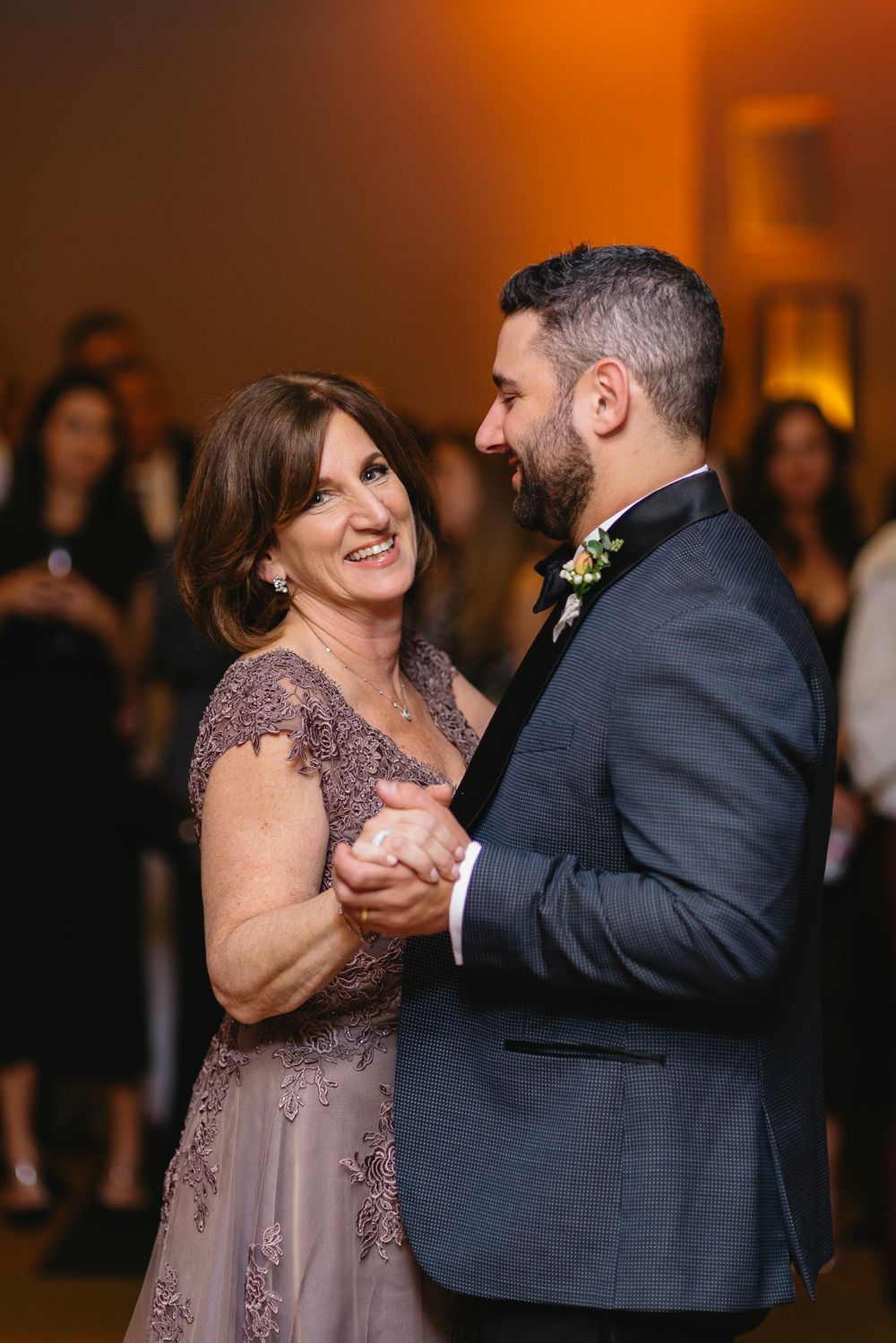 A couple shares a joyful dance moment in formal attire at a wedding reception with warm amber lighting.