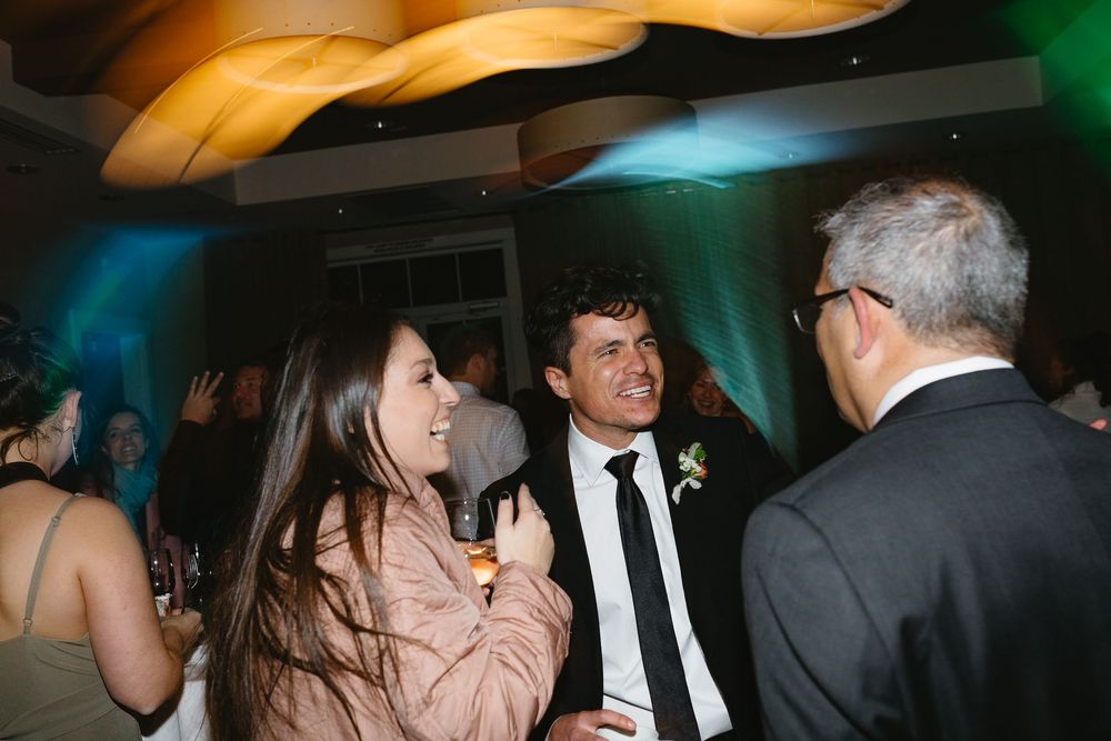 People dancing and celebrating at a dimly lit wedding reception with warm lighting and festive atmosphere.